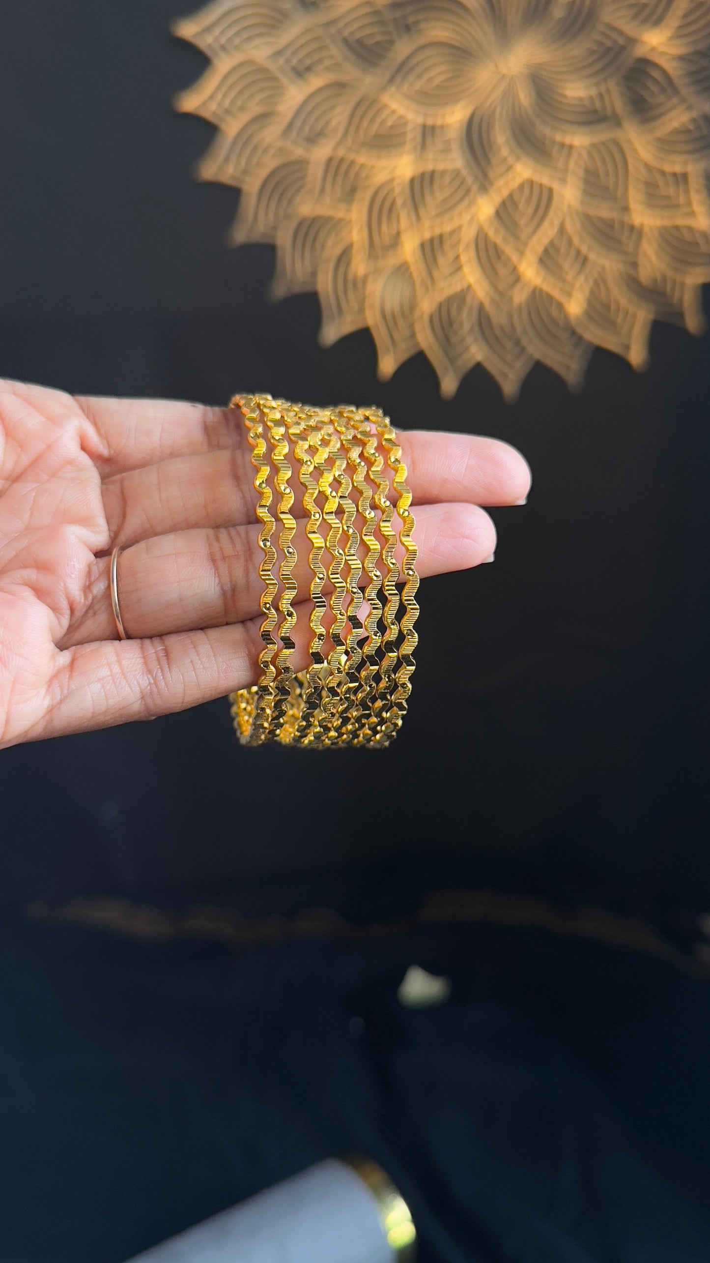 Gold bracelet on a hand with a decorative gold design in the background