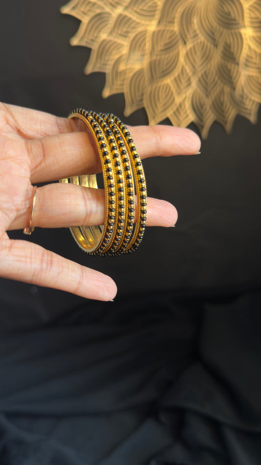 Gold bangles on a hand with a black background