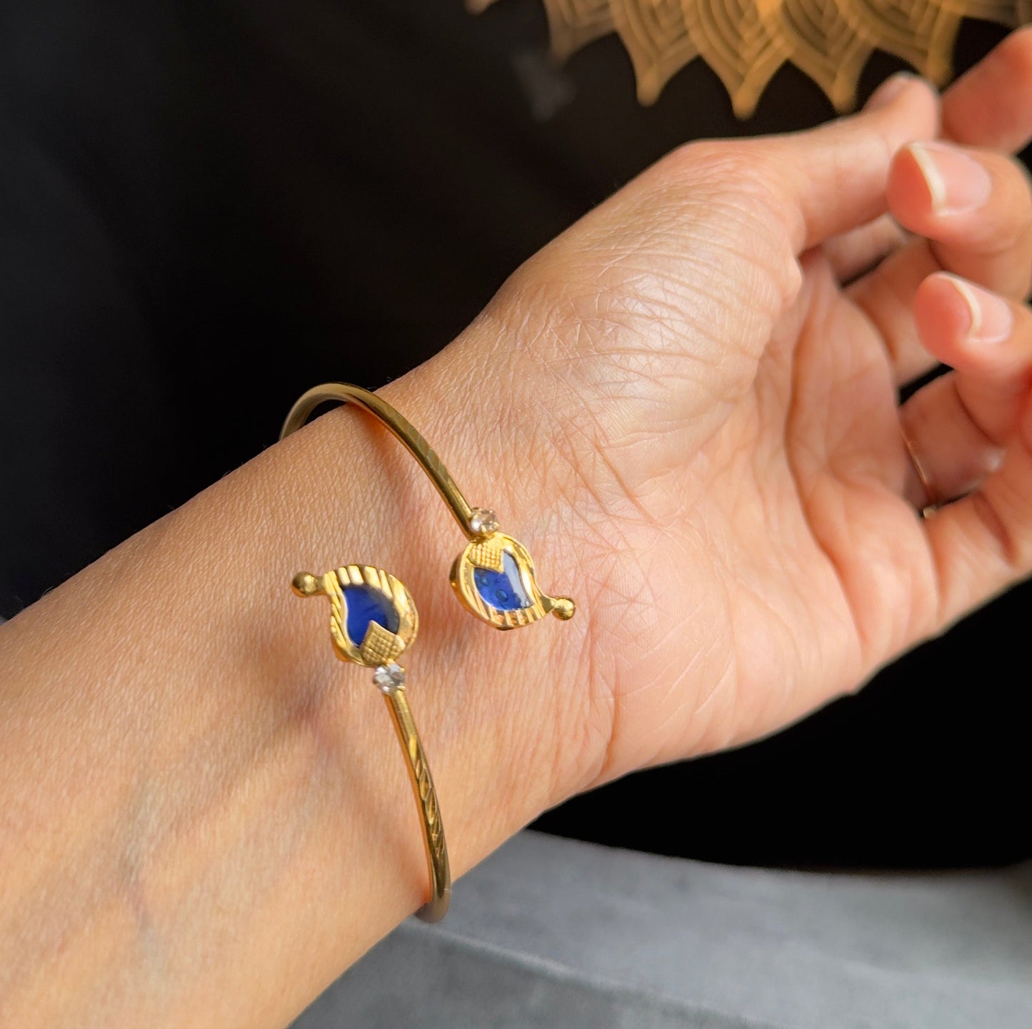 Hand wearing a gold bracelet with a blue stone against a dark background