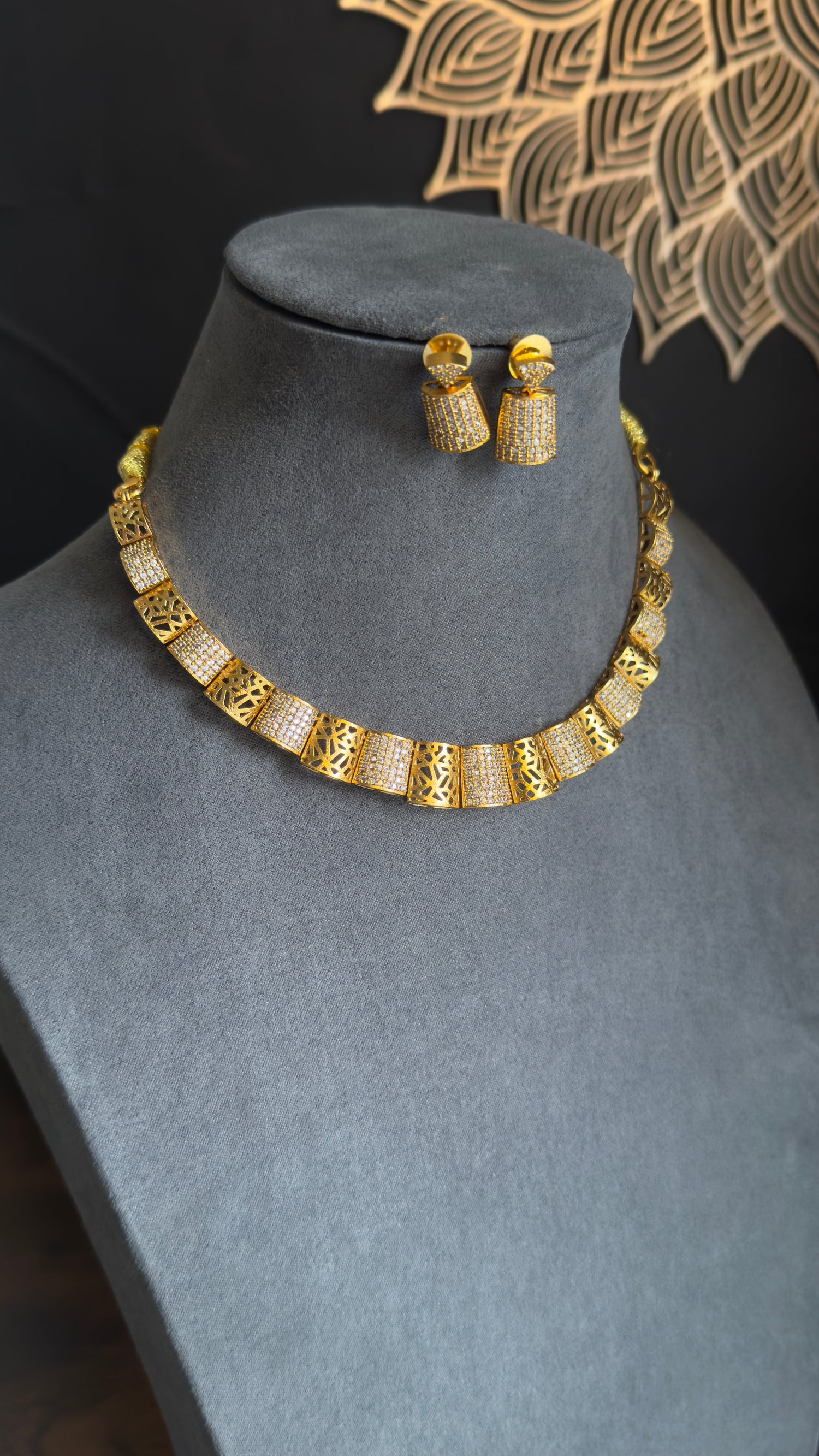 Gold necklace and earrings set on a gray mannequin bust with a dark background