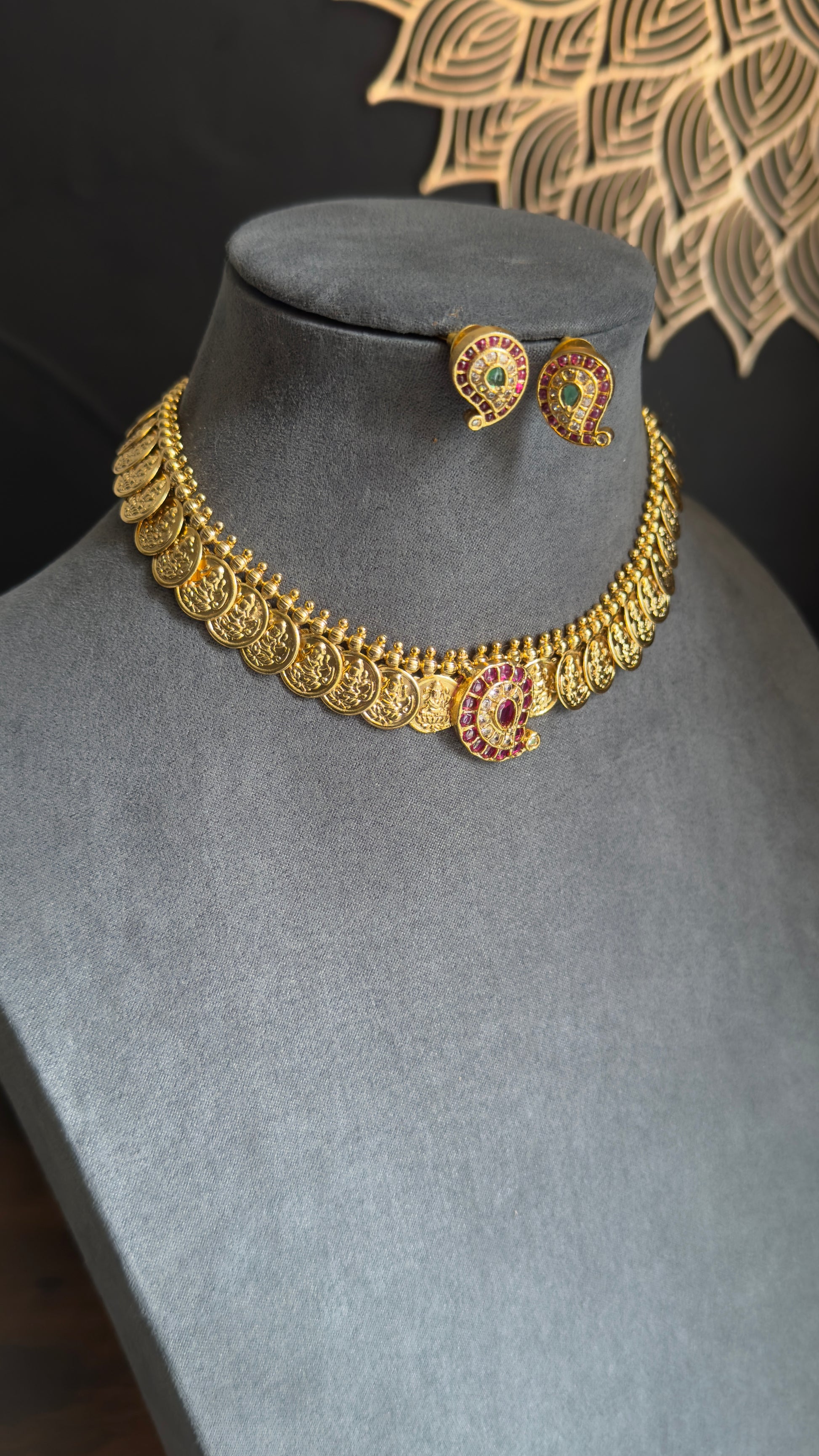 Gold necklace and earrings on a mannequin bust with a decorative background