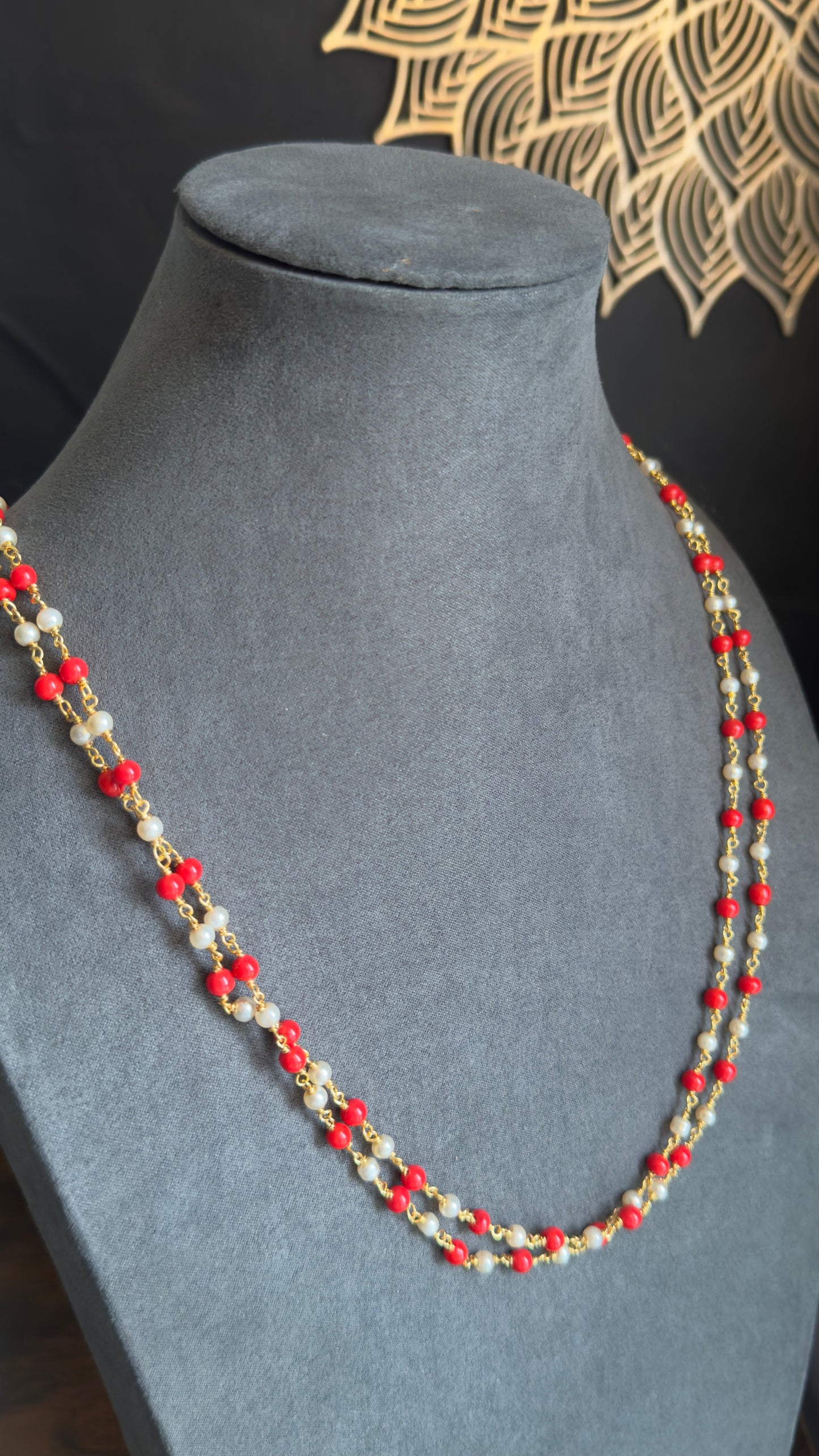 Necklace with red and gold beads on a gray mannequin bust against a black background.