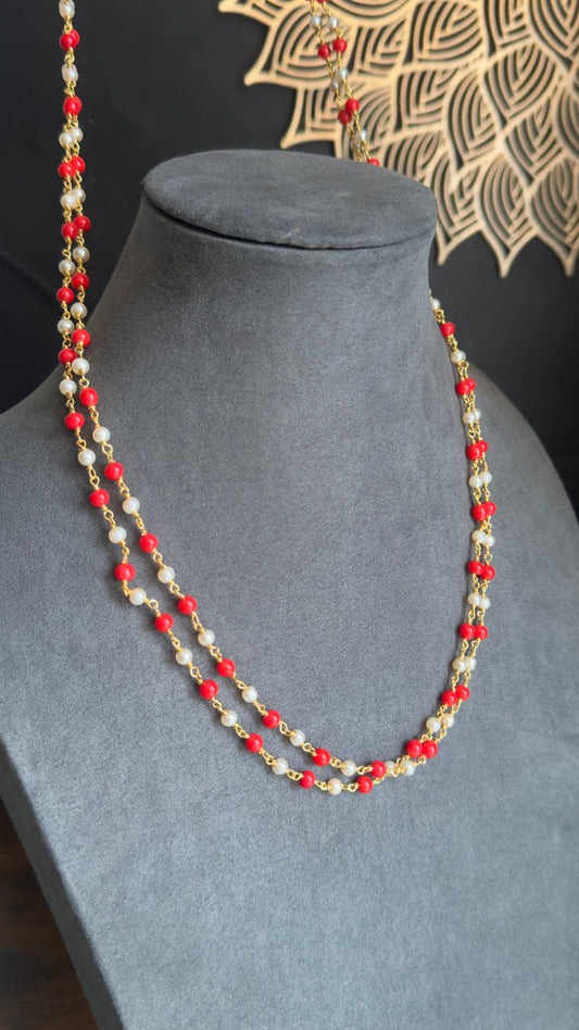Beaded necklace with red, white, and gold beads on a gray mannequin against a black background.