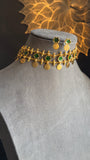 Gold necklace with green accents on a mannequin bust, with a decorative gold background.