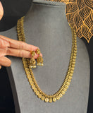 Gold necklace on a gray stand with a hand touching it