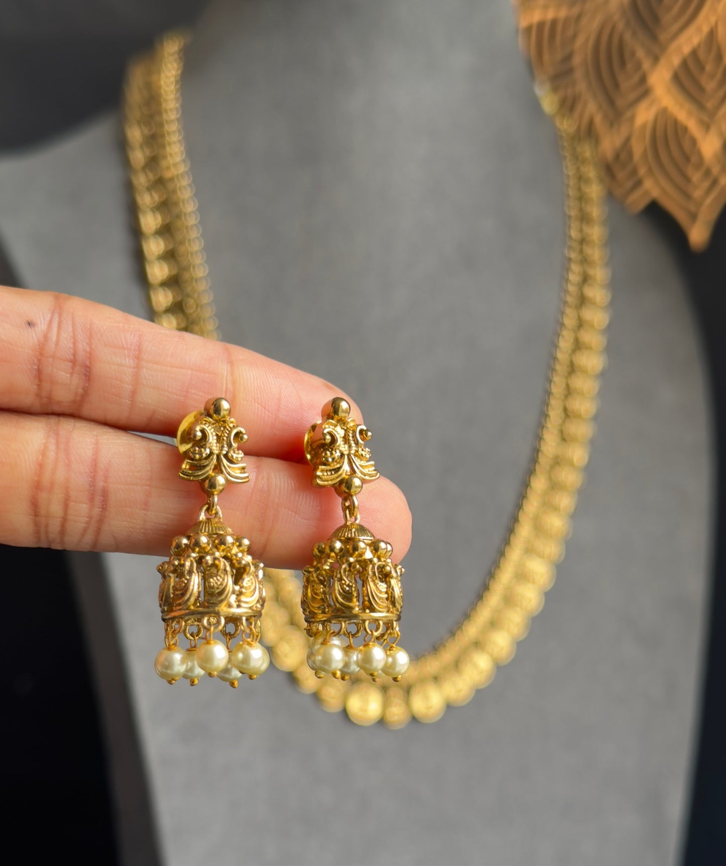Gold earrings with pearl details held by a hand against a gray background