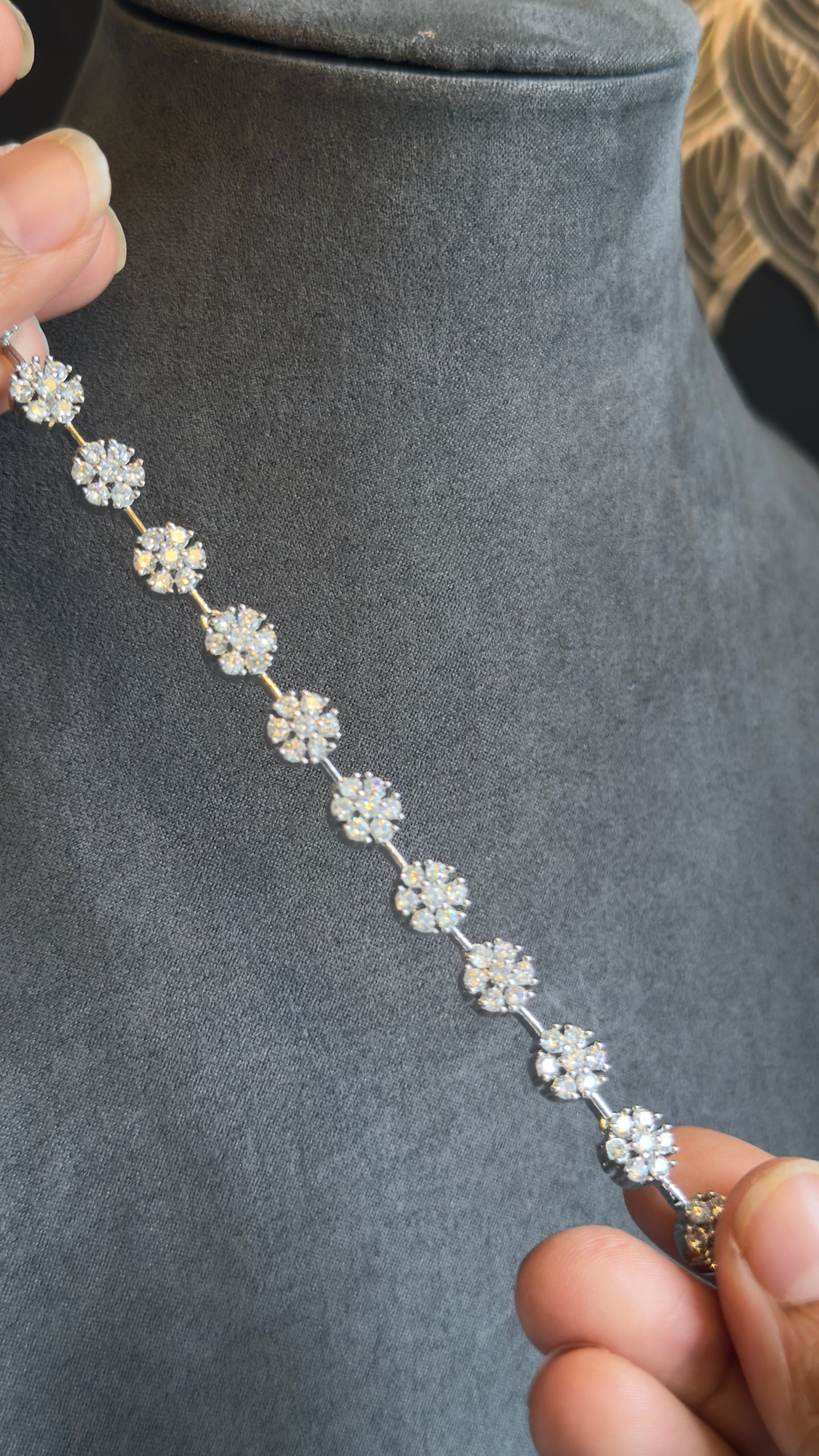 Silver floral bracelet held by a hand on a gray mannequin