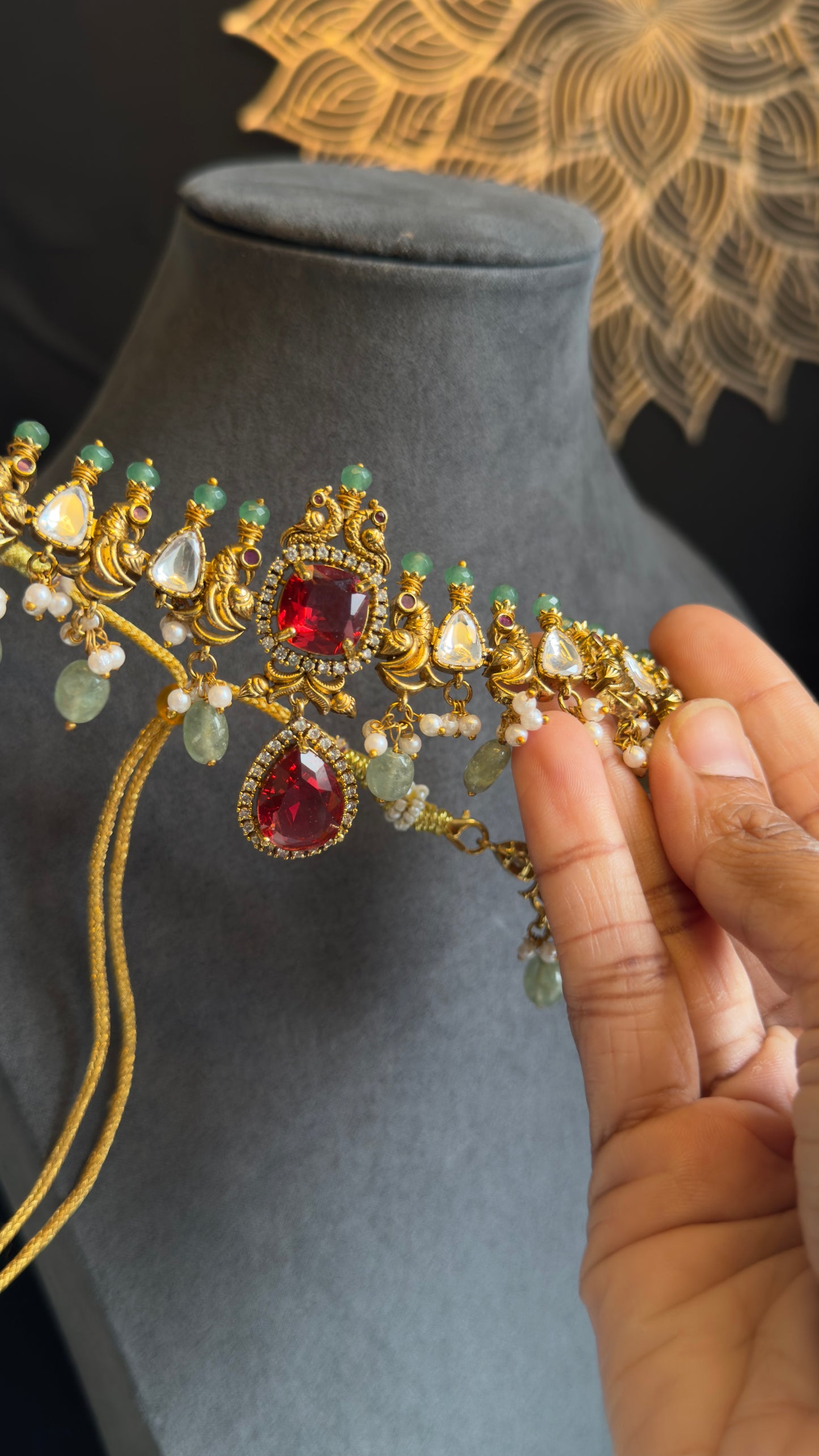 Gold jewelry with red and green gemstones held by a hand on a gray surface.