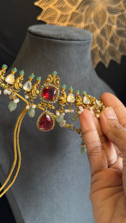 Gold jewelry with red and green gemstones held by a hand on a gray surface.