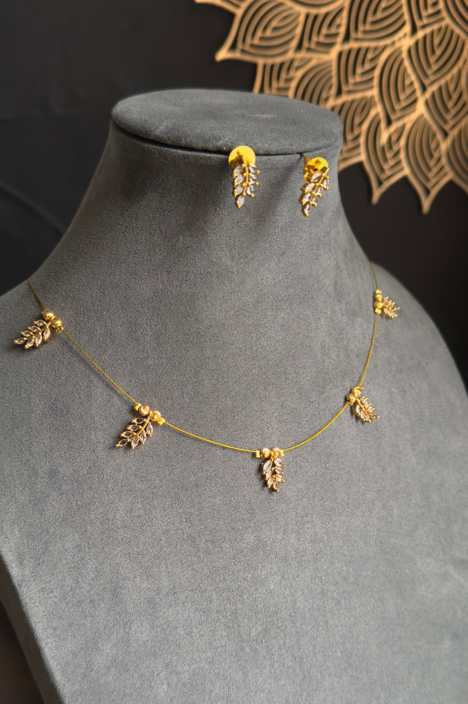 Gold necklace and earrings on a gray mannequin bust with a decorative background.