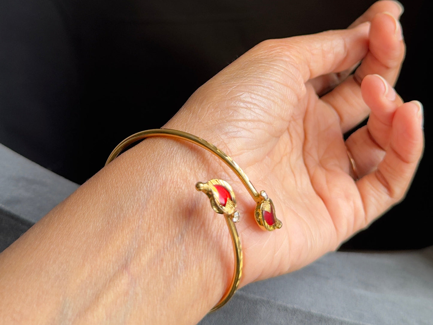 Hand wearing a gold bracelet with a red gemstone against a black background