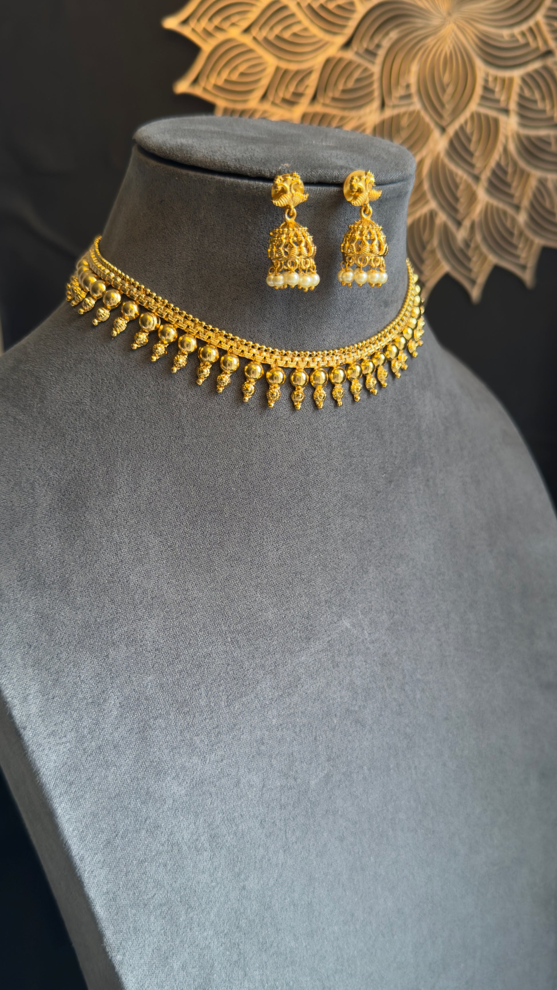 Gold necklace and earrings on a mannequin bust with a decorative background