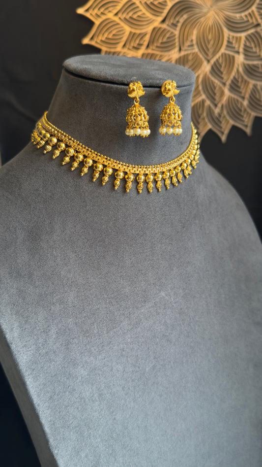 Gold necklace and earrings on a mannequin bust with a decorative background