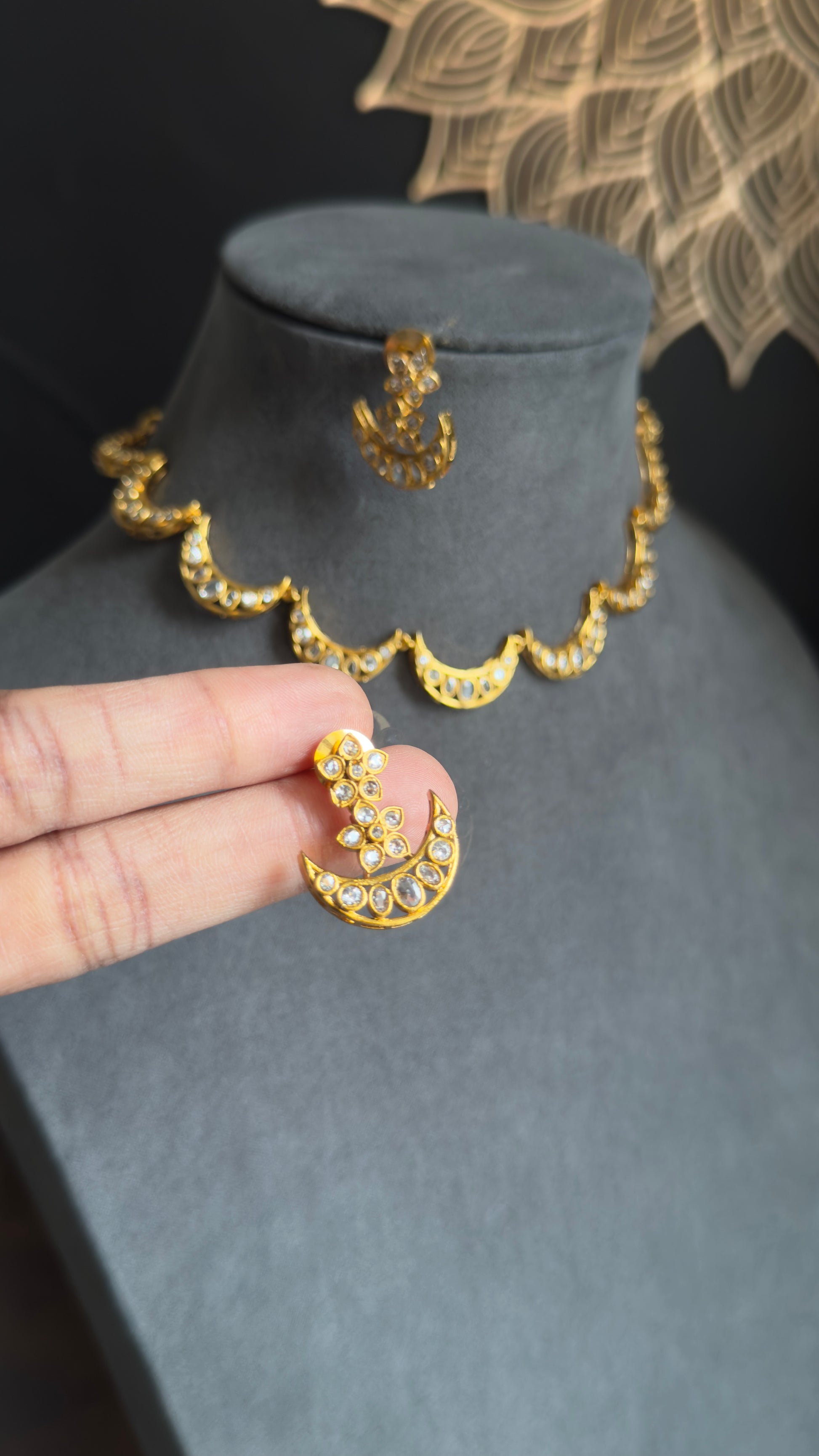 Gold necklace and earrings on a black mannequin with a hand holding an earring.