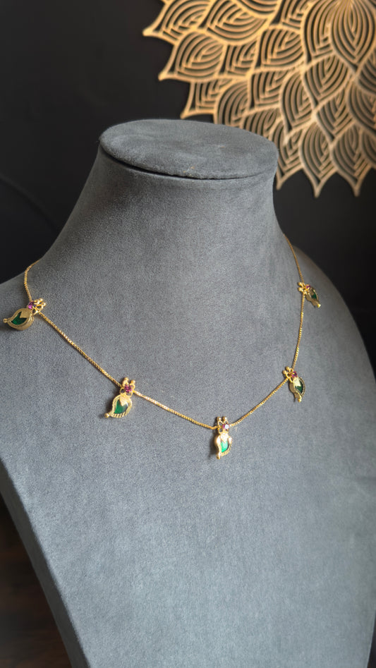 Gold necklace with green gemstones on a gray mannequin bust against a black background