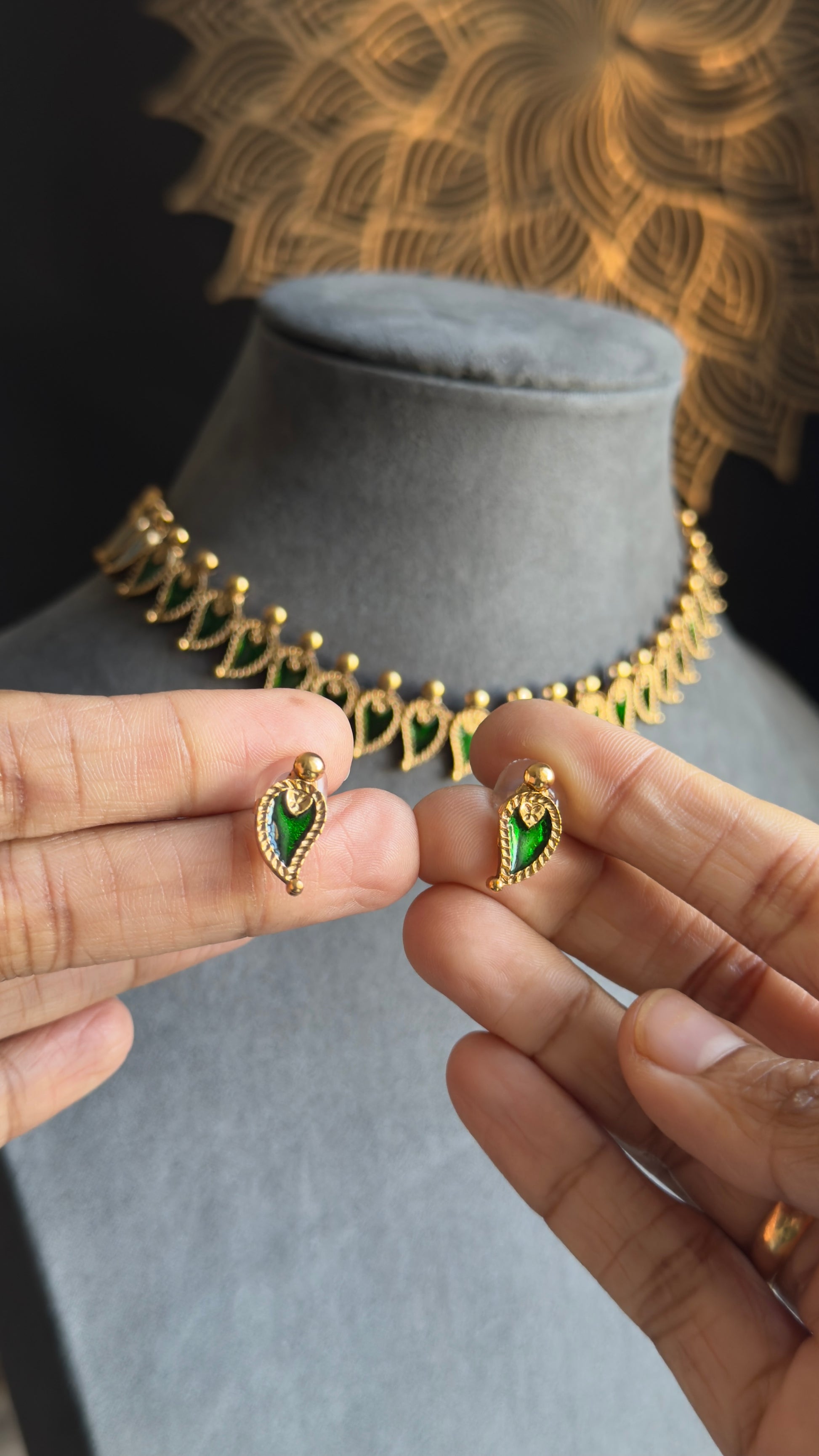 Gold earrings with green gemstones held by hands, necklace in the background