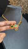 Gold necklace with green gemstones held by a hand on a gray mannequin bust.