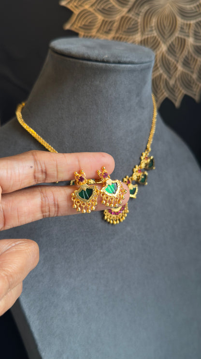 Gold necklace with green gemstones held by a hand on a gray mannequin bust.