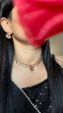 Close-up of a person wearing a necklace with a blurred red flower in the foreground