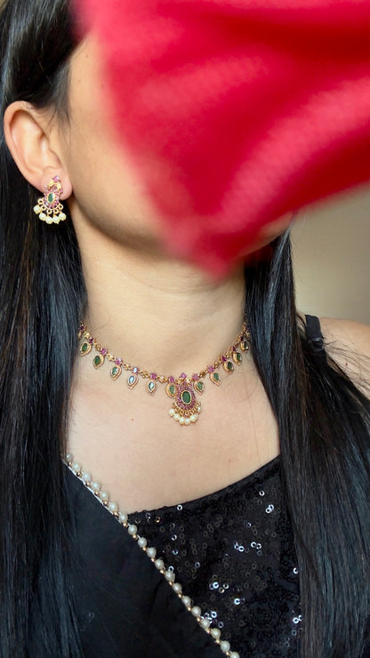 Close-up of a person wearing a necklace with a blurred red flower in the foreground
