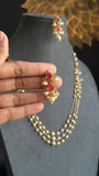 Pearl necklace with red gemstones held by a hand against a dark background