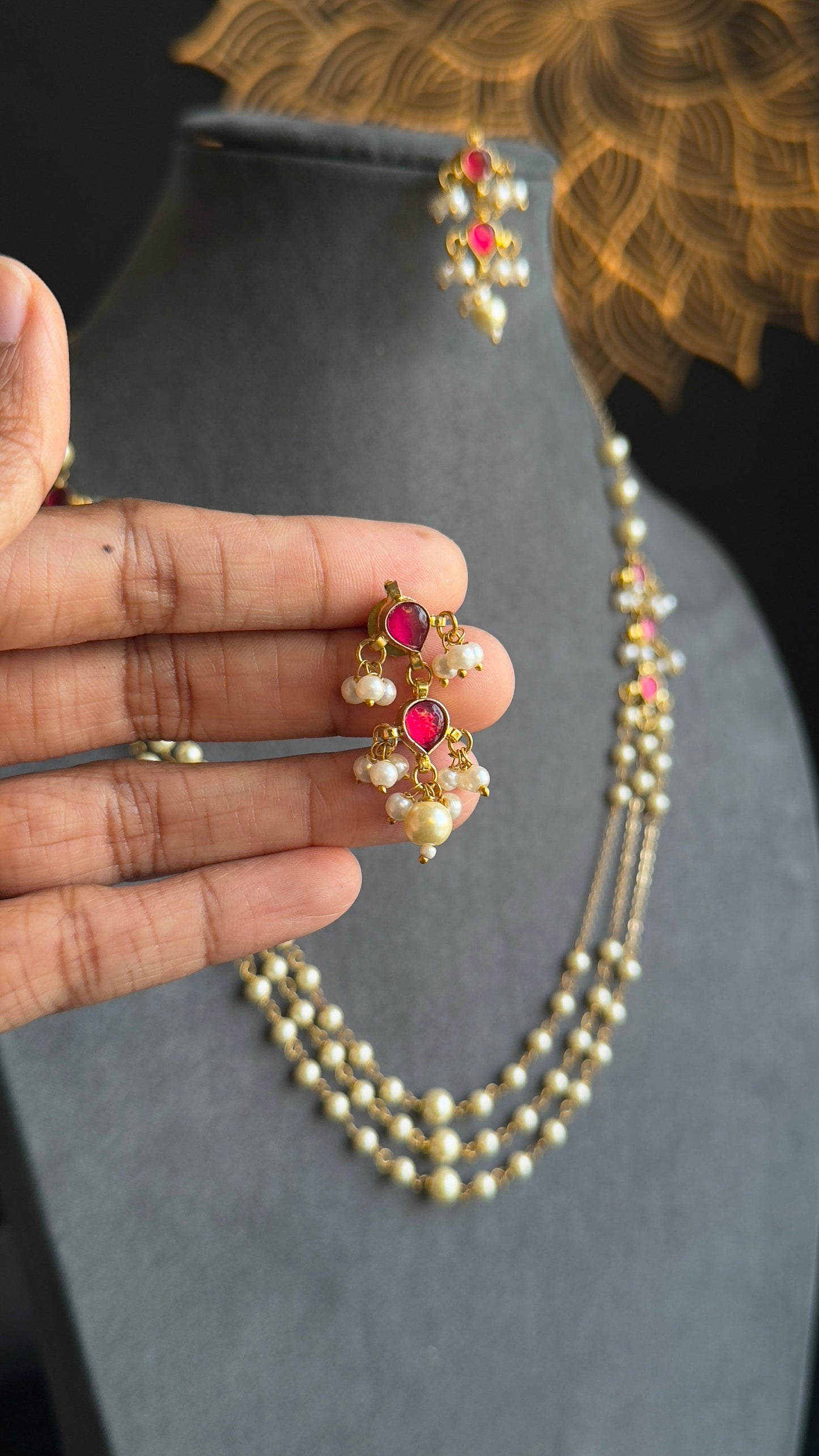 Pearl necklace with red gemstones held by a hand against a dark background