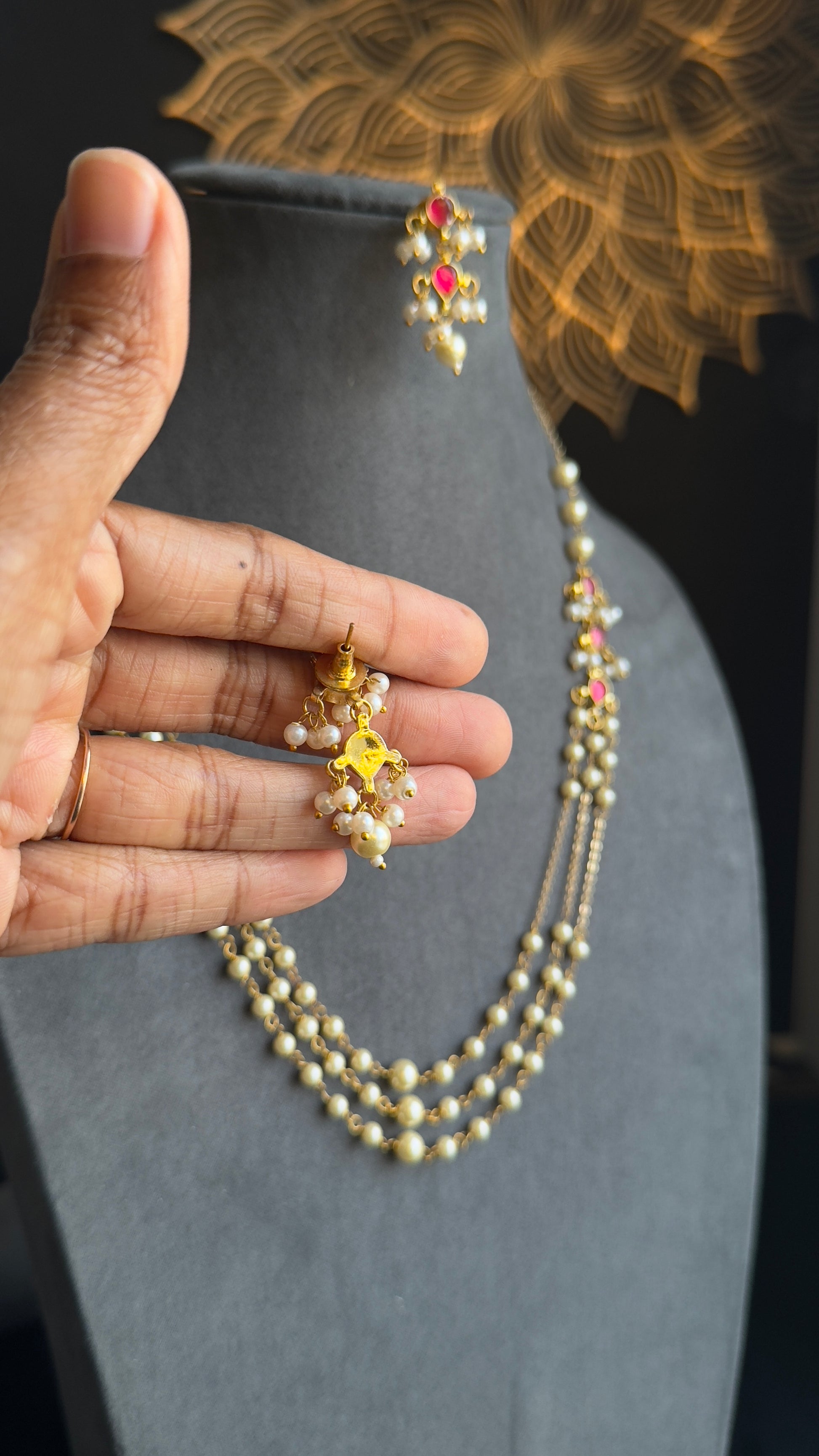 Hand holding a pearl necklace with a decorative background