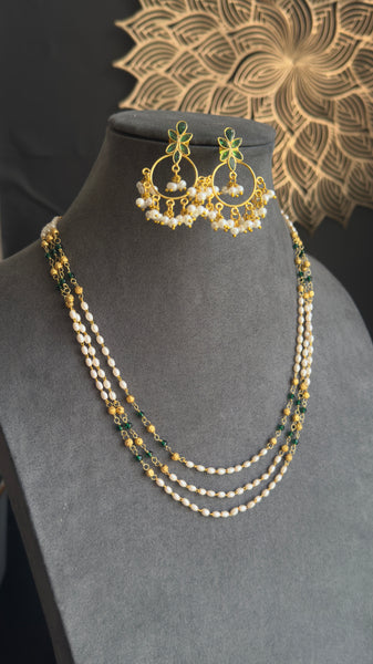 A three-layered pearl and bead necklace set with matching gold-toned earrings, displayed on a gray jewelry bust against a dark background with a decorative mandala motif.