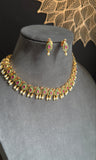 Gold necklace with green and red stones on a mannequin bust against a dark background.