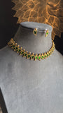 Gold necklace with green stones on a mannequin bust against a decorative gold background