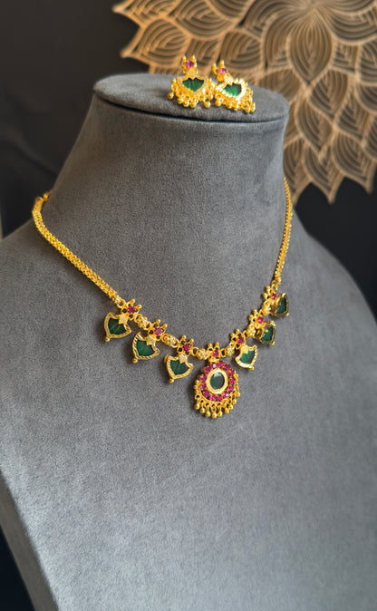 Gold necklace with green and red gemstones on a gray mannequin bust.
