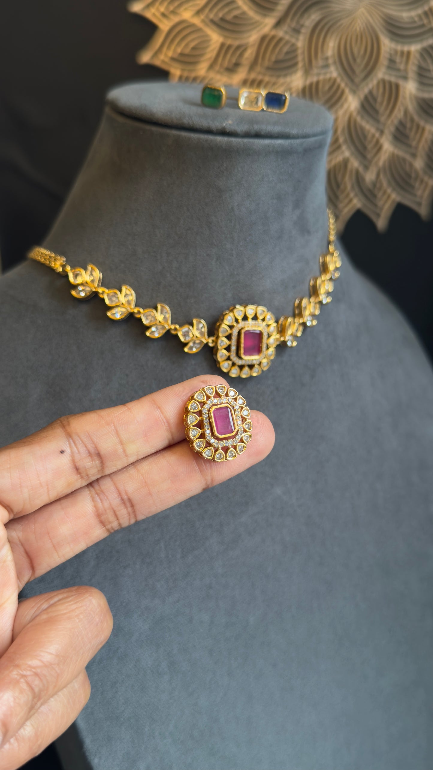 Gold necklace and earrings held by a hand on a gray mannequin with a decorative background.