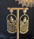 A pair of gold-toned traditional Indian chandbali earrings with bird motifs and dangling bead chains, displayed on a gold stand against a dark background.
