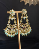 A pair of ornate gold-toned dangle earrings with clear stones, light blue beads, and small pink gemstone accents, displayed on a gold stand against a dark background.