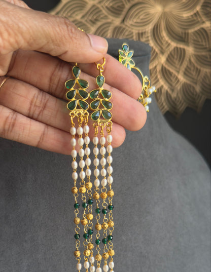 A hand holding a gold and green beaded tassel necklace with matching earrings against a gray background.