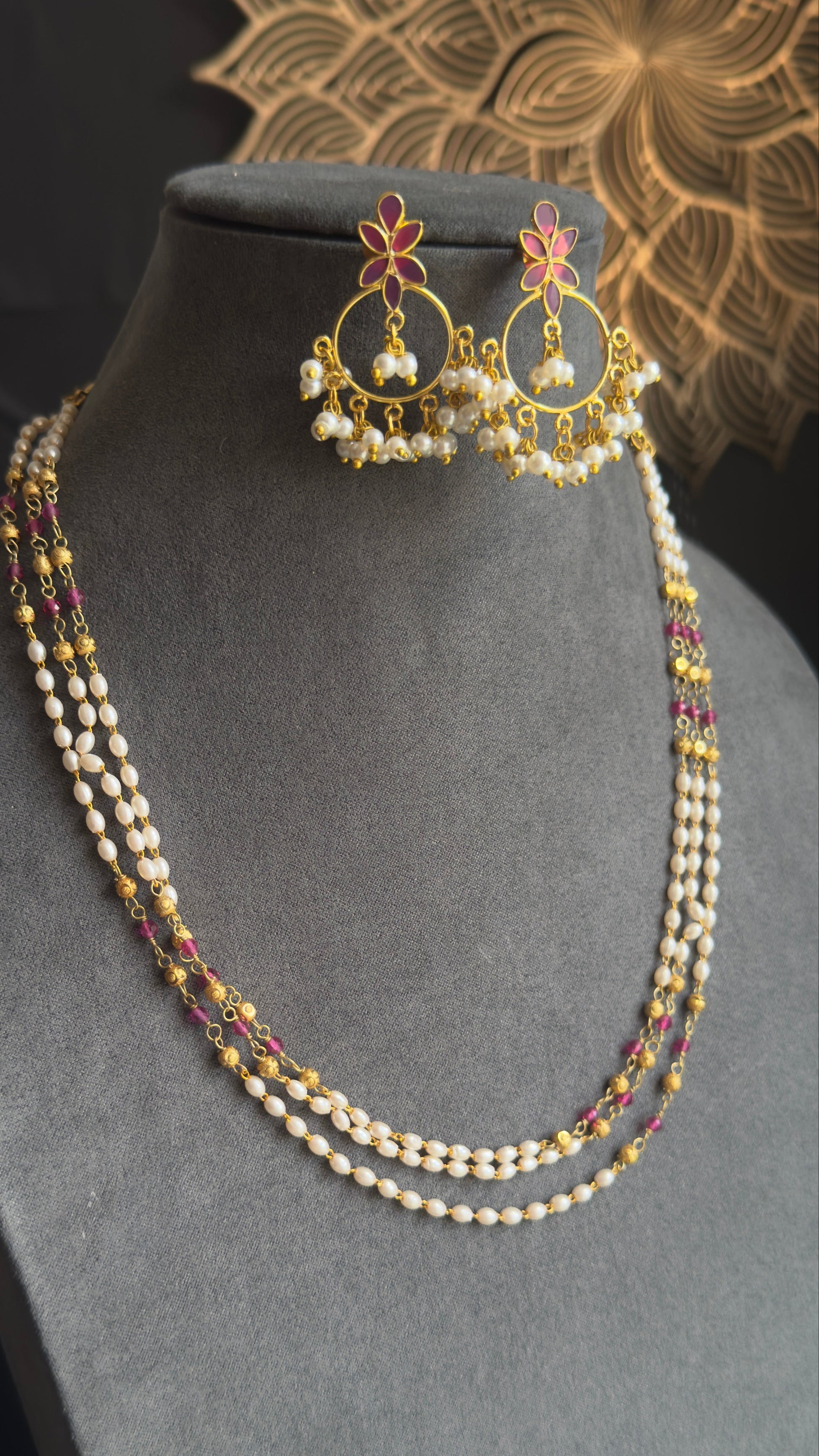 A gold and pearl jewelry set displayed on a gray velvet mannequin bust, featuring a multi-strand necklace with white pearls and gold accents, matching drop earrings, and a small matching piece resting above the bust.