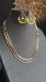 A gold-plated traditional Indian jewelry set featuring a multi-strand necklace with white pearls and red stones, matching drop earrings, and a matching headpiece, displayed on a gray velvet mannequin bust.