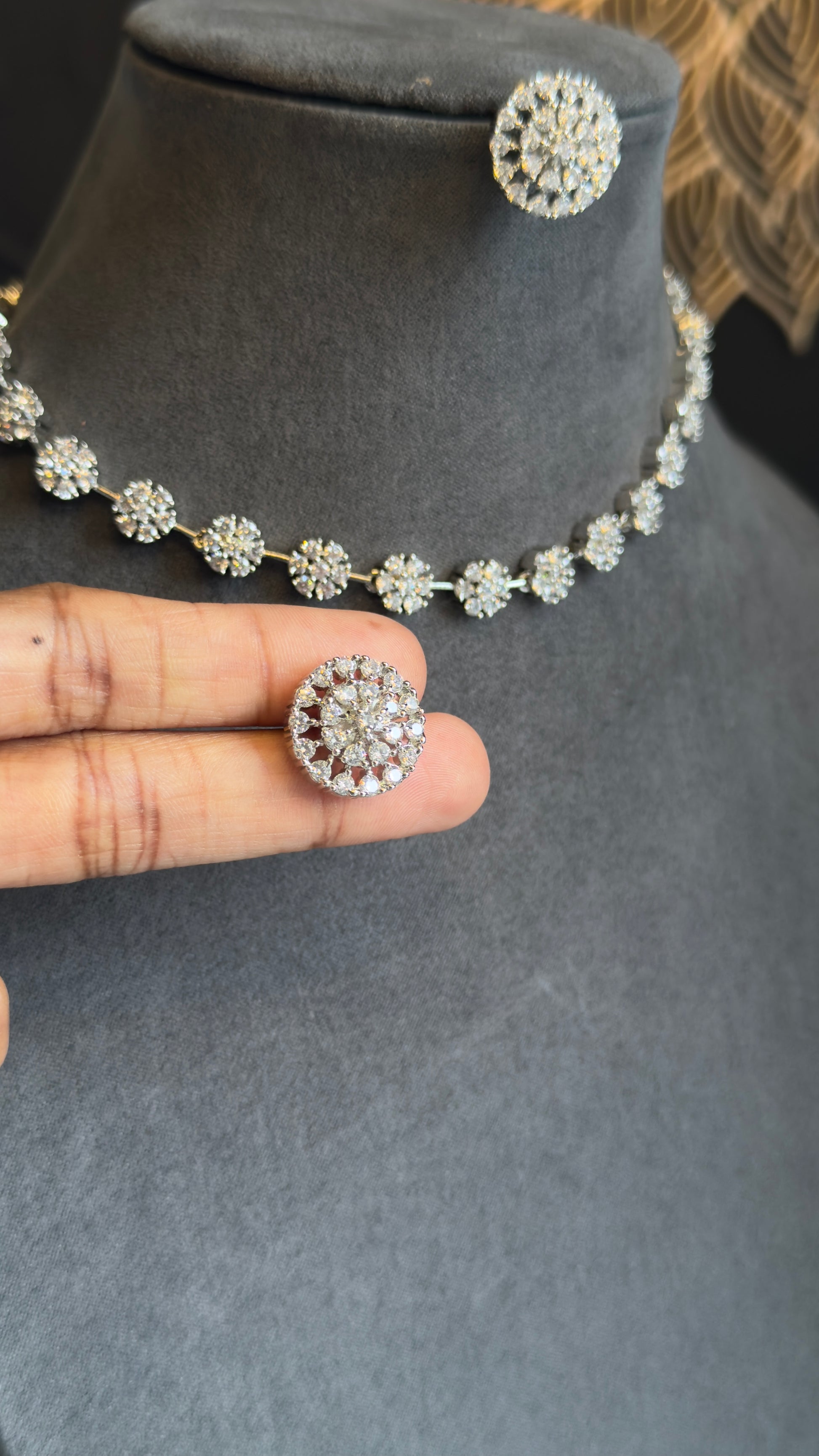 Silver necklace and earrings on a mannequin bust with a hand holding one earring.