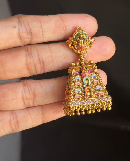 A hand holding a small gold-toned jhumka earring decorated with colorful enamel and bead details, against a dark clothing background.