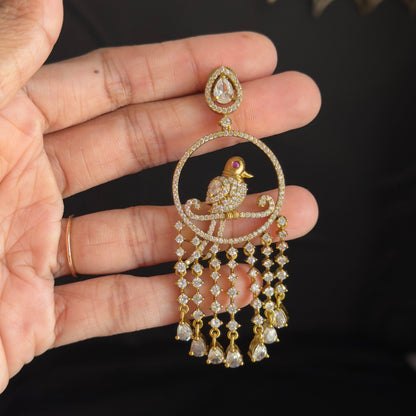 A gold-toned statement dangle earring with a bird motif and clear stones, held in a person's hand against a dark background.